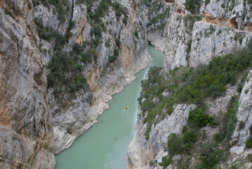 Path carved into the rock of the Mont-Rebei canyon, in the Montsec saw, in Lleida, and below on the water a kayak crosses the river.