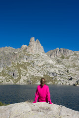Fototapeta premium A backpacker woman in a pink jacket sitting outdoors on a rock in front of the lake, contemplate the needles of the mountain. Epic vacations and adventure in the Aigüestortes National Park. Back view.