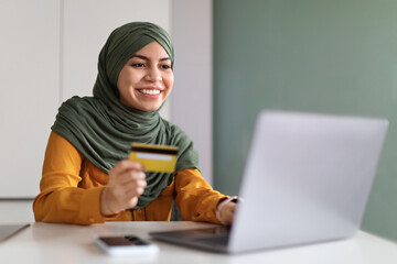 Online Payments. Smiling Muslim Woman In Hijab Using Laptop And Credit Card