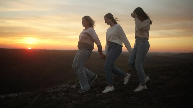 Mother with her daughters are walking on a mountain top at sunset