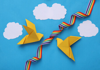 Yellow origami doves with rainbow ribbon on a blue background. Peace symbol, no war