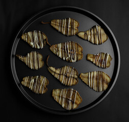dried pears decorated with white and black chocolate and sesame seeds on a black tray and a dark background. for postcards menu labels calendars signs and stands