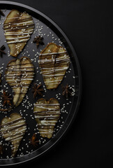 dried pears decorated with white and black chocolate and sesame seeds on a black tray and a dark background. for postcards menu labels calendars signs and stands