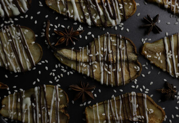 dried pears decorated with white and black chocolate and sesame seeds on a black tray and a dark background. for postcards menu labels calendars signs and stands