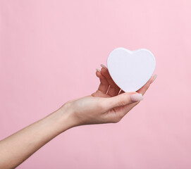Obraz premium Woman's hand holding a heart-shaped box on a pink background