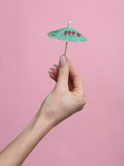Woman's hand holding a cocktail umbrella on a pink background