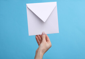 Woman's hand holding white envelope on a blue background