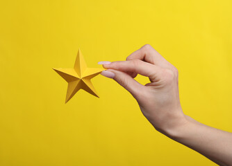 Woman's hand holding a paper star on a yellow background