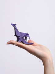 Female hand holds origami Dragon on white background. Hobby, creativity