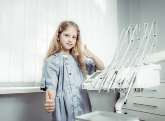 Little girl shows thumbs up at the dental clinic. Dental Pediatrics