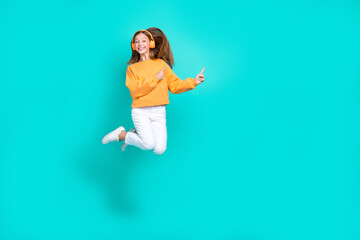 Full length photo of pretty shiny schoolgirl wear orange sweatshirt headphones jumping empty space isolated turquoise color background