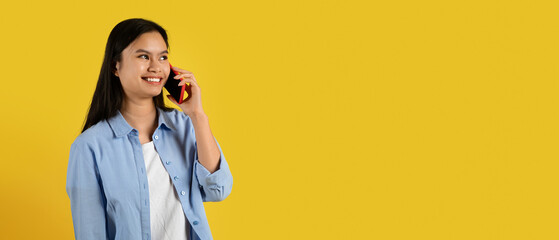 Glad cute millennial korean female in casual calling by smartphone, talking with friend, look at...