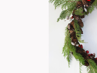 a semicircle of a christmas wreath of fir cones, red berries, silvery acorns and green coniferous branches on a light background with space for text
