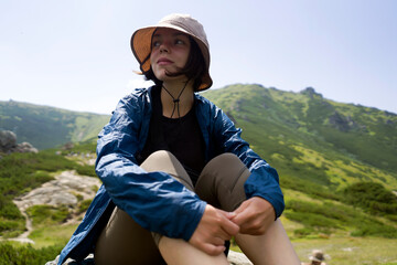 Girl in a hat enjoys her journey, sitting on the rock. © Zhanna