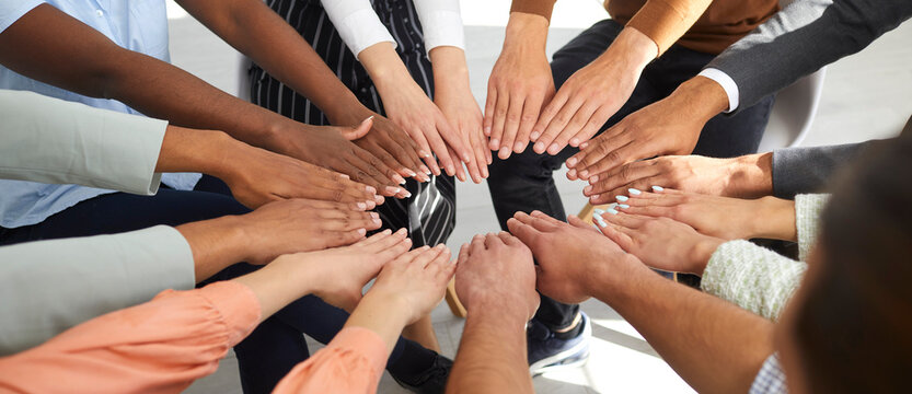 Multiracial men and women put their hands together in circle as symbol of cooperation and unity. Unrecognizable people sitting in circle each holding out two hands. Human support concept. Close up.