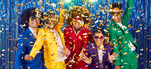 Group of energetic funny friends who are having fun and dancing together in confetti at disco party. Young people in colorful suits laugh out loud against backdrop of shiny foil curtain. Banner. - Powered by Adobe
