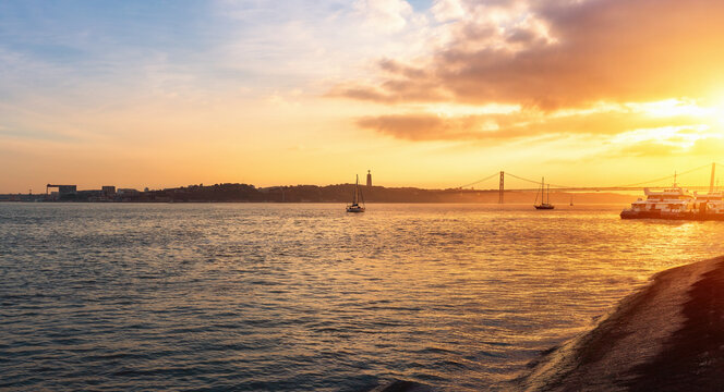Tagus River (Rio Tejo) at sunset with 25 de Abril Bridge and Sanctuary of Christ the King on background - Lisbon, Portugal