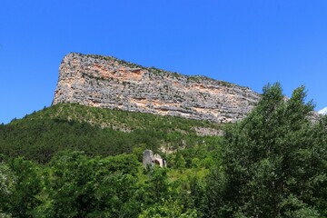 View of a cliff surrounded by green vegetation. Rocher du Caire, Remuzat, France.