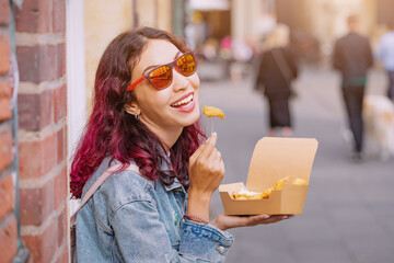 Cheerful happy girl eating fast food meal with shrimp in batter on the city street with a takeaway...