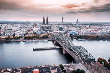 Koln Aerial view with trains move on a bridge over the Rhine River on which cargo barges and passenger ships ply. The majestic Cologne Cathedral in the background