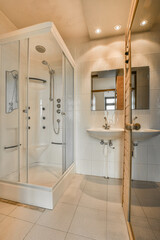 Shower faucets attached to tiled wall near glass partition and finnish wooden sauna in washroom at...