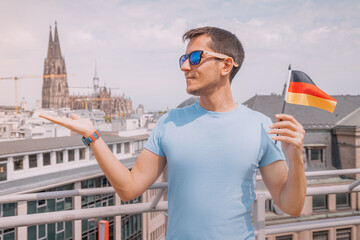 Happy man with a German flag against the roofs of the old town and Cologne cathedral. Patriotism and traditional holidays