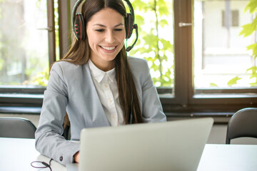 Young businesswoman with headset working on laptop in modern office.