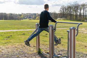 Sweden, Knislinge – April 29, 2022: A young man doing sport exercises, training in outdoor gym on a sunny day in spring or autumn. Street workout