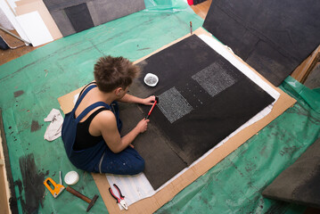 Young woman artist creating contemporary art piece made of black canvas and nails