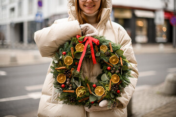 beautiful wreath decorated with dry orange slices balls and ribbon in female hands