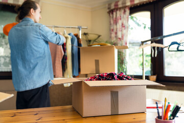 Box with pre owned clothes for resale or donation, unfocused man on background preparing the clothes.