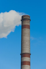 Pollution of the environment, ecology and air. Withdrawal of combustion products of soot, smoke and gases from the pipe of an industrial plant into the atmosphere against the background of a blue sky