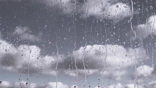 Rain Drops Flow Down Glass Against a Background of Moving Clouds and Grey Sky. Time-lapse. Slow-moving cumulus clouds. Rainy weather. Streams of water flow down the window on glass. Meteorology.