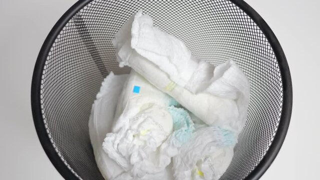 Parent throws used diapers taking care of baby health and ecology at home. Person changes nappy and takes care of baby hygienic throwing diapers into bin
