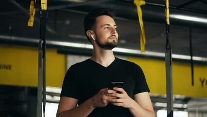 Cheerful man using earbuds listening to music in fitness club, motivational mood