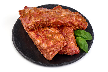 Raw marinated pork ribs on black stone plate ready for cooking, isolated on white background.