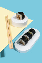 Hosomaki (sushi, rolls) with eel on a white plaster stand on a multi-colored plain background (blue, yellow).