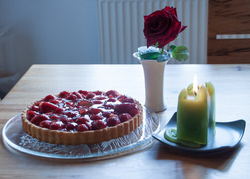 &Uuml;berraschung frische Erbeertorte mit Kerzenlicht und einer roten Rose zum Geburtstag auf einem K&uuml;chentisch