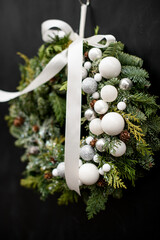 Close-up of beautiful natural wreath of spruce and thuja branches decorated with white balls and ribbon