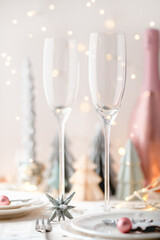 Xmas table settings in white and pink colors with trendy paper christmas trees on background, empty plates and glasses ready for festive dinner and party