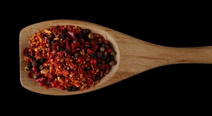 Spicy mixture of spices with chopped lemon peel, chili, peppercorns (black, green and red), mustard seeds, allspice, chopped ginger in wooden spoon isolated on black, top view