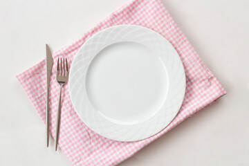 Empty white plate with pink fabric napkin, a fork and a knife on white table. Top view.