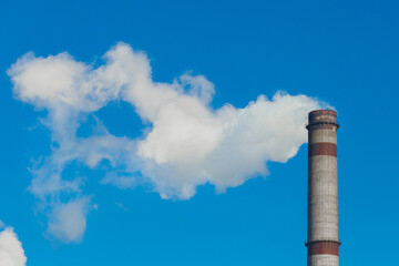 Pollution of the environment, ecology and air. Withdrawal of combustion products of soot, smoke and gases from the pipe of an industrial plant into the atmosphere against the background of a blue sky