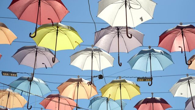 Street scenery from open multi-colored umbrellas suspended above ground to decorate city and create shade from hot summer sun. Urban art object with parasols protecting from sunlight under blue sky