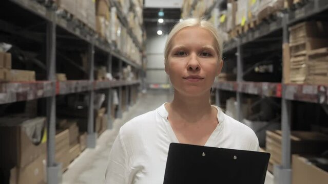Business concepts. European women are smiling with confidence in the warehouse. A blonde woman in a white shirt smiles at the camera standing in a warehouse with documents in her hands. 4k footage