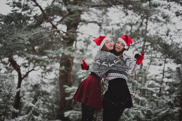 Two young teenage hipster girl friends together.Close up fashion portrait of two sisters hugs and having fun winter time,wearing red santa hats and sweater,best friends couple outdoors, snowy weather