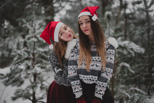 Two young teenage hipster girl friends together.Close up fashion portrait of two sisters hugs and having fun winter time,wearing red santa hats and sweater,best friends couple outdoors, snowy weather