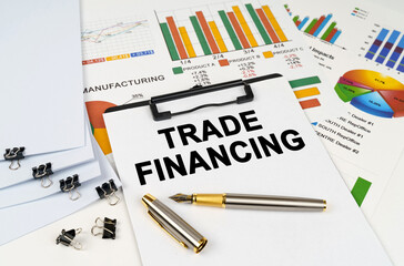On the table among financial graphs and charts lies a tablet with the inscription - TRADE FINANCING