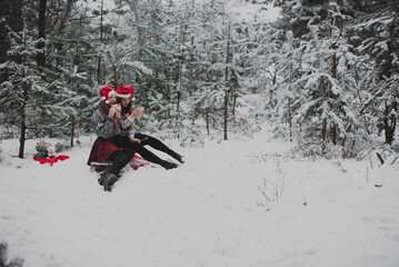 Close up fashion portrait of two sisters hugs and having fun, drinking tea winter time,wearing red santa hats and sweater,best friends couple outdoors, snowy weather