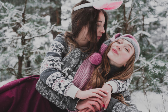Close up fashion portrait of two sisters hugs and having fun winter time,wearing pink hats, rabbit ears and sweater,best friends couple outdoors, snowy weather